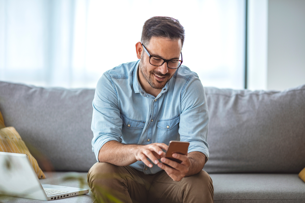 Middle aged man sat down whilst learning how to unlock iPhone 4 device online. 