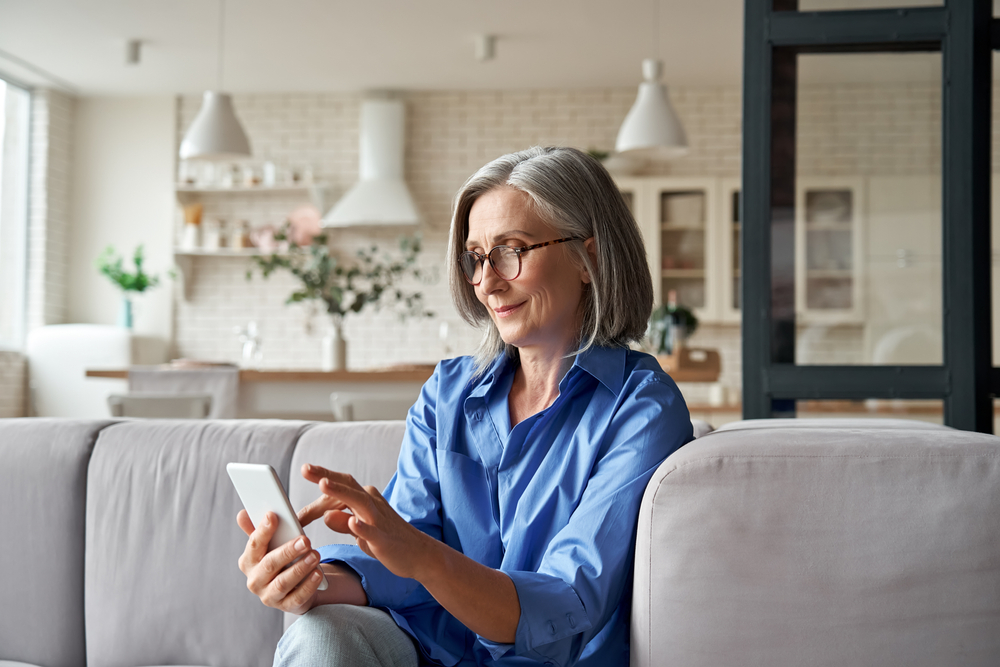 Mature lady sat on her sofa looking at her unlocked iPhone 5S screen.