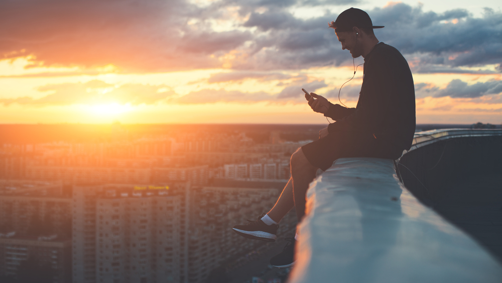 Young man sat on a roof top whilst using his phone that has an iCloud check unlock.