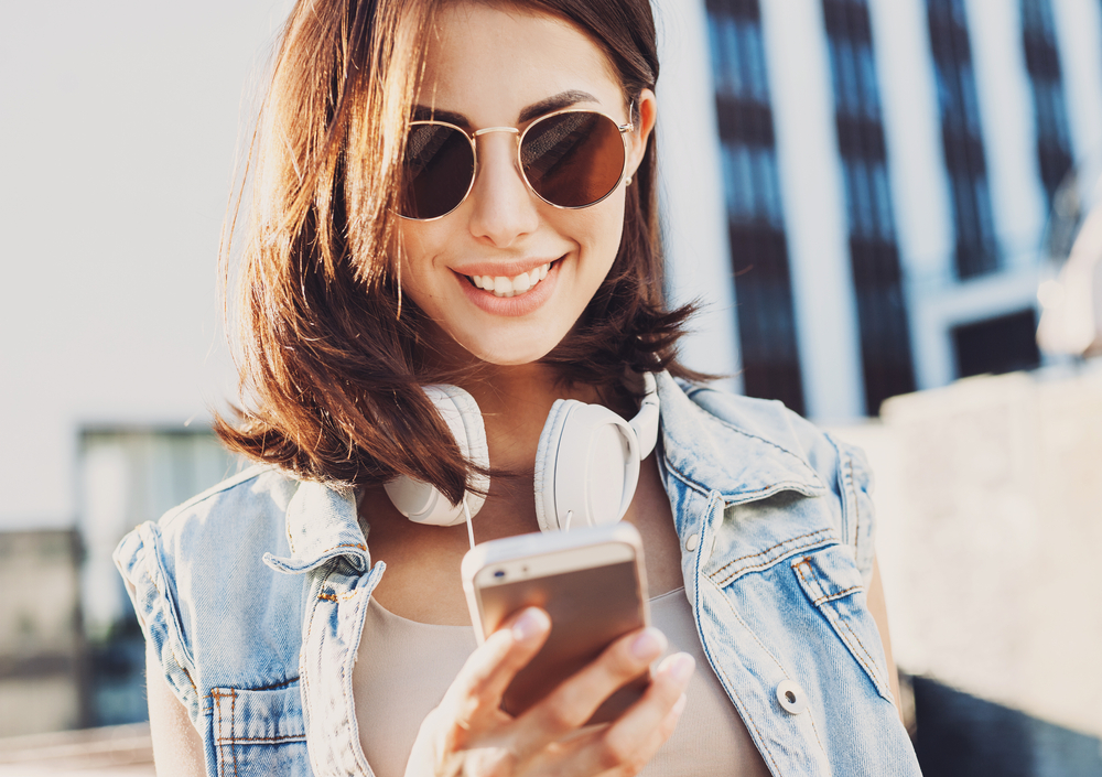 Young brunette woman wearing sunglasses whilst getting an IMEI check from Mobile Unlocked.