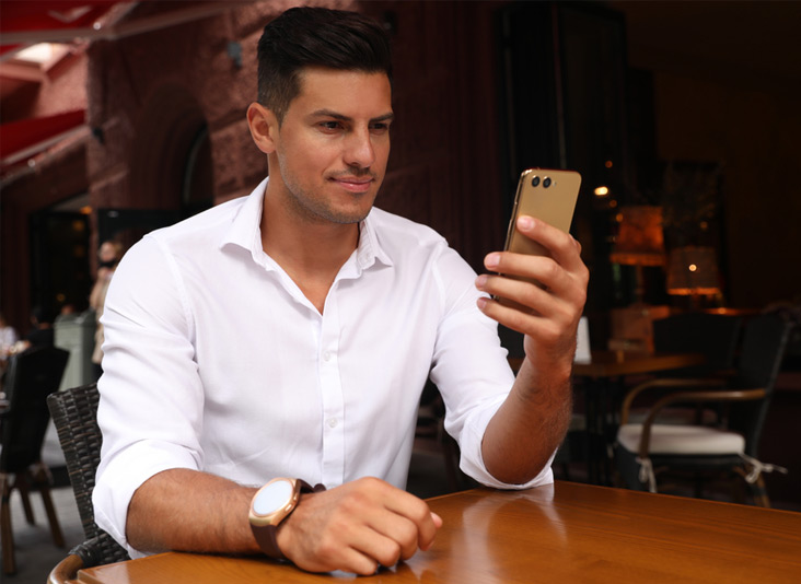 Young professional man sat at a table whilst holding his unlock Simple mobile phone. 