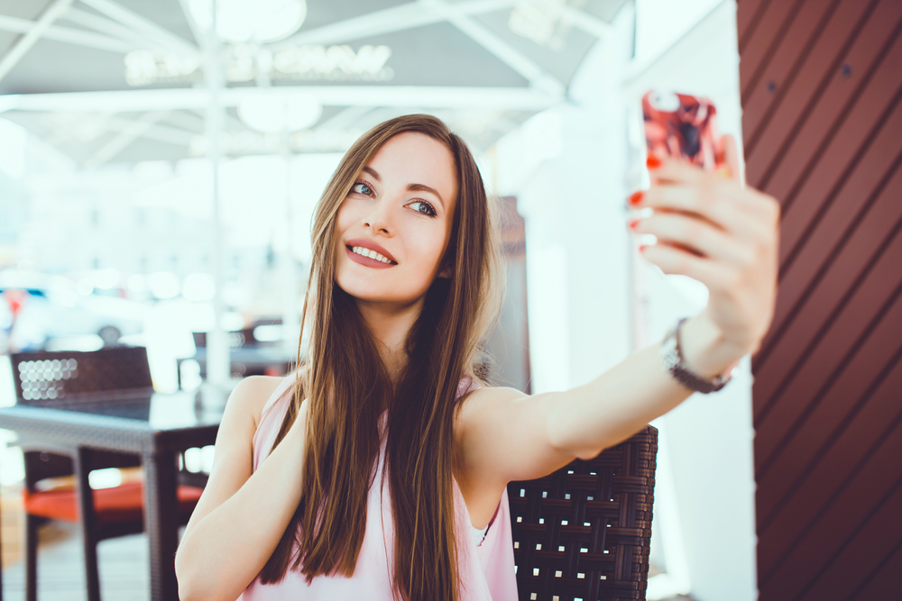 Sassy young woman taking a selfie on her iPhone 12 Pro Max that she unlocked online.